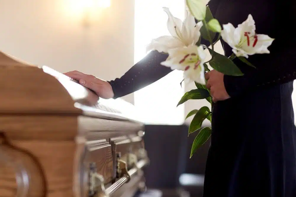 Woman with flowers touching a casket - CGH Injury Lawyers