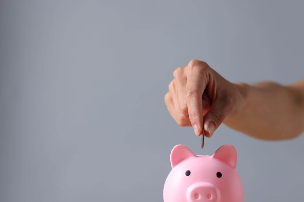A hand dropping a coin into a pink piggy bank - CGH Injury Lawyers