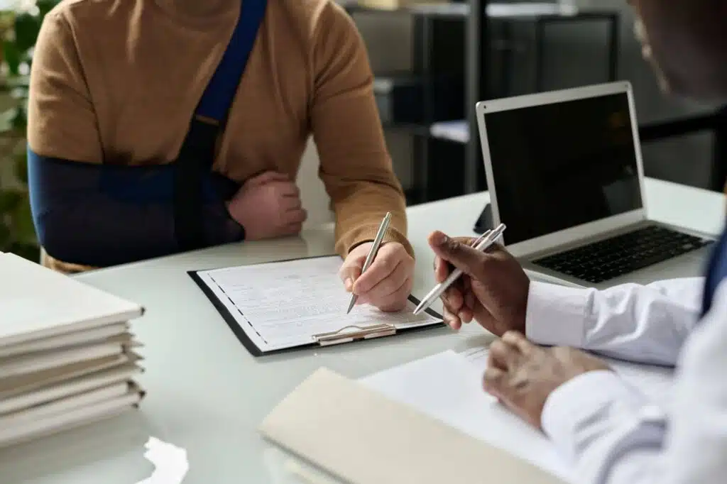 Man with his arm in a sling signing a form at a desk