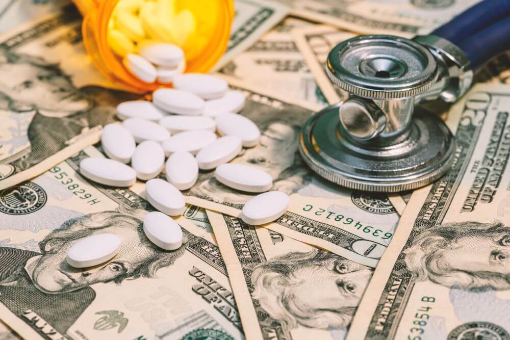 White pills and a stethoscope lying on twenty-dollar bills - CGH Injury Lawyers