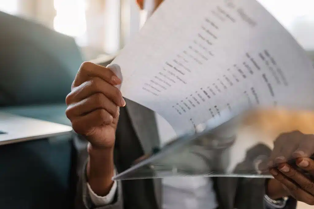 A person in a gray blazer reading a printed statement with rows of dollar amounts